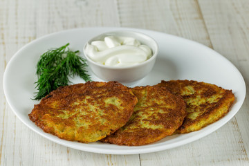 Potato pancakes on a white plate with sour cream