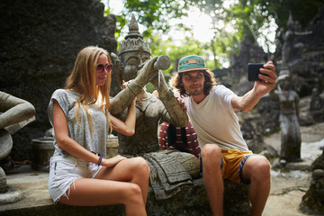Naklejka premium tourist couple taking selfie with ancient buddhist statue in thailand
