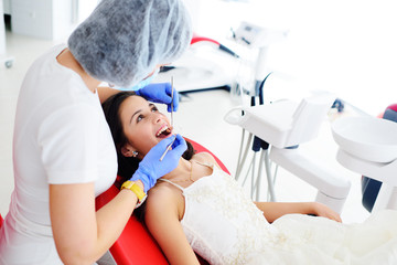 Obraz na płótnie Canvas Dentist girl treats teeth to baby girl in smart dress in red dental chair