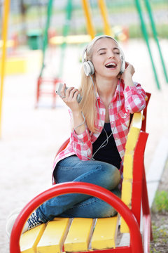 Young beautiful woman with headphones sitting on the bench and listening to music outdoors