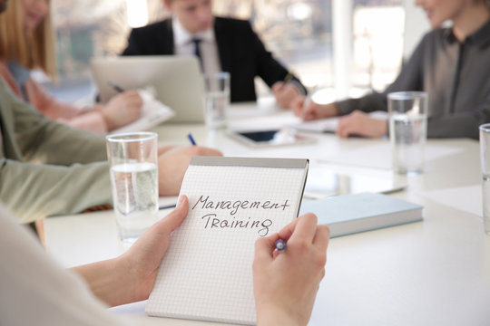 Woman holding notebook with text MANAGEMENT TRAINING at business presentation