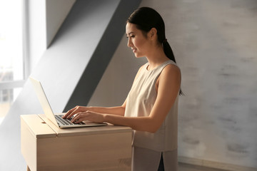 Asian woman typing on laptop at stand-up workplace