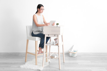 Asian woman with tablet computer sitting at high desk in room
