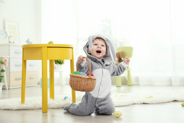 Fototapeta premium Cute little baby in bunny costume playing with Easter eggs at home