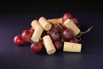 Many wine corks and a vintage cork screw and red grape on a dark background