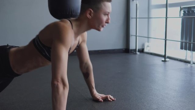 A young athlete makes push-ups in the fitness club from the floor to strengthen the biceps and triceps. A woman crossed her legs to increase the load on her arms and dorsal complex.