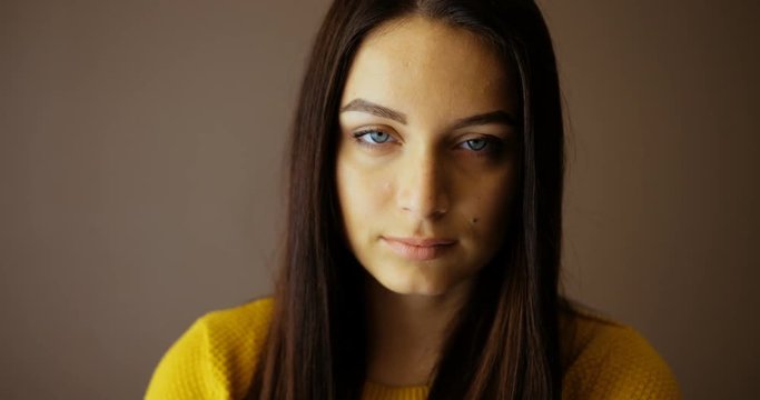 Close up portrait of beautiful young woman looking at the camera indoor. Pretty woman in yellow sweater. Close-up portrait shot. Serious face