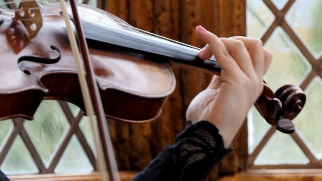 Close up of woman's hands playing violin near vintage style diamond glass window