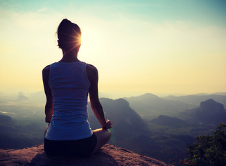 young fitness woman meditating on sunrise mountain peak