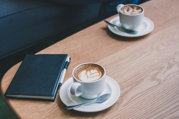 Coffee cup with note book on wooden table background with vintage filter