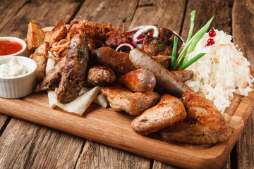 Grilled meat and sausages with tasty sauces, potato wedges and sauerkraut served on rustic wooden table. Restaurant menu photo.