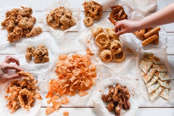 Appetizing fresh beer snack assortment on white wooden table, flat lay. Junk food, unhealthy eating, calories. Unrecognizable person take pieces, dining, buffet