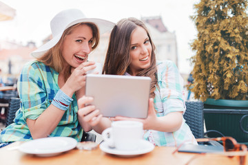 Two beautiful women sitting in the cafe after shopping, drinking coffee and having fun with tablet. Consumerism, lifestyle concept