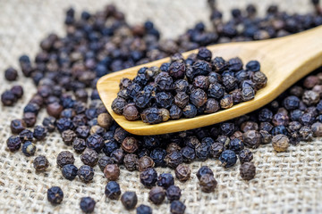 Black pepper seeds in wooden spoon.