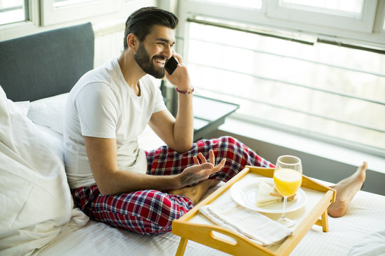 Young Man Having Breakfast In Bed And Using A Mobile Phone