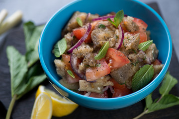 Close-up of a blue bowl with baked eggplants, fresh tomatoes and mint salad, shallow depth of field