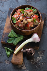 Rustic wooden serving board with baked aubergines and fresh tomatoes salad, brown stone background