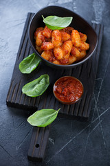 Potato gnocchi with red pesto sauce on a black wooden serving board, studio shot