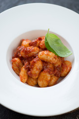 Close-up of potato gnocchi served with red pesto sauce and fresh basil