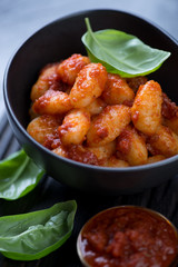 Closeup of black ceramic bowl with italian potato gnocchi served with red pesto, selective focus