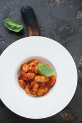 White glass plate with potato gnocchi with red pesto, top view over brown stone background
