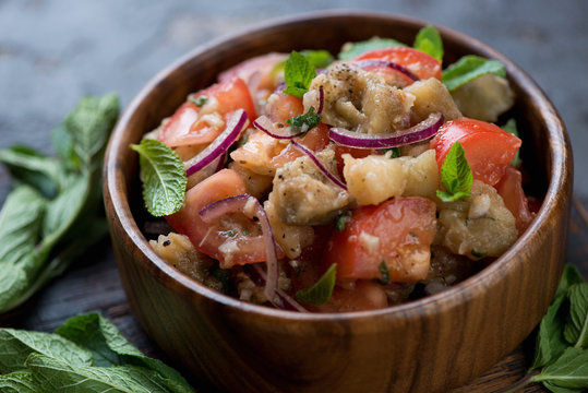 Salad with baked eggplants, fresh tomatoes and mint in a wooden bowl, close-up