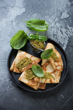 Frying pan with flapjacks and basil pesto topping, elevated view over grey stone surface