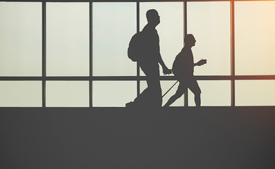 Fototapeta na wymiar Travellers in airport walking to departures by escalator in front of window silhouette