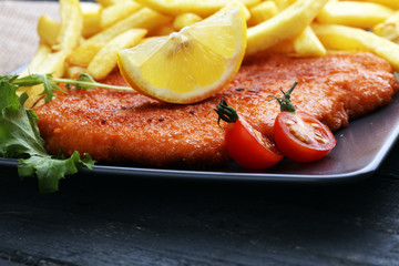 Dish of Wiener schnitzel and French fries served with sauces and salad on rustic wooden table