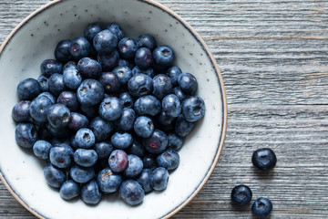 Fresh blueberries in a bowl over rustic wooden background. Top view, copy space