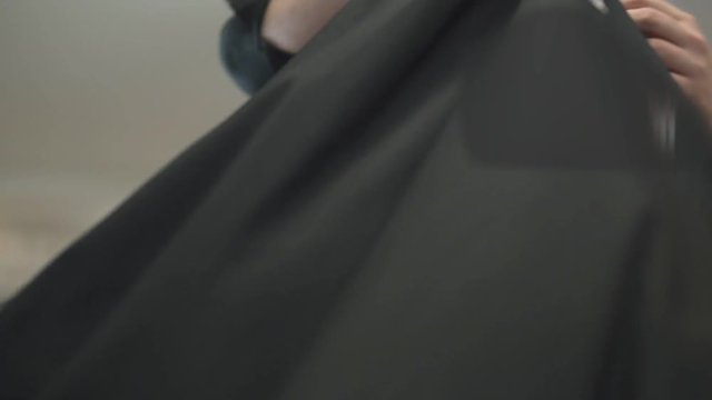 Beautiful woman with short brown hair sitting in a chair in a hair salon while a hairdresser taking out black protective cape from her and taking away small hairs using brush. Shot in slowmotion.