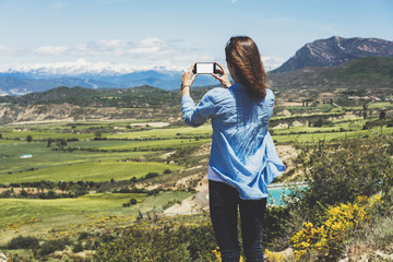 Fototapeta na wymiar Hipster photograph on smart phone gadget mobile, mock up of blank screen. Girl traveler hold in hand mobile on background mountain landscape horizon. Tourist look map on trip, lifestyle concept