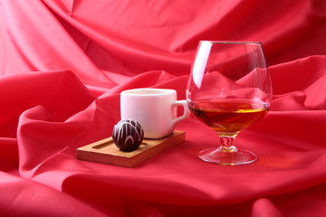 White cup of coffee and cognac in a glasses, pralines on red background.