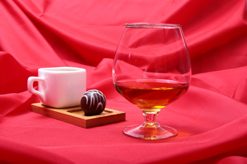 White cup of coffee and cognac in a glasses, pralines on red background.