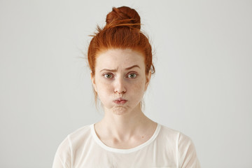 Annoyed irritated young red-haired female with freckles blowing her cheeks, frowning, feeling...