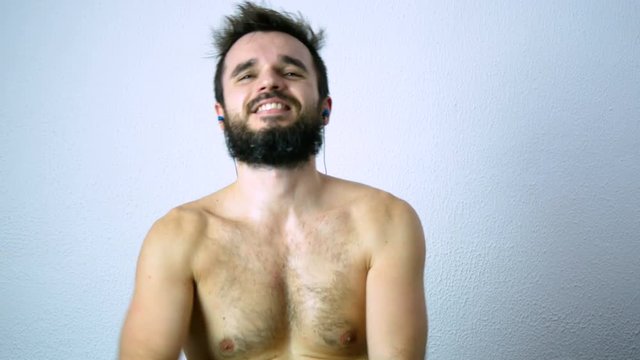 Vigorous self-confident bearded naked man enjoying trap hip-hop music after a workout, isolated on white background.