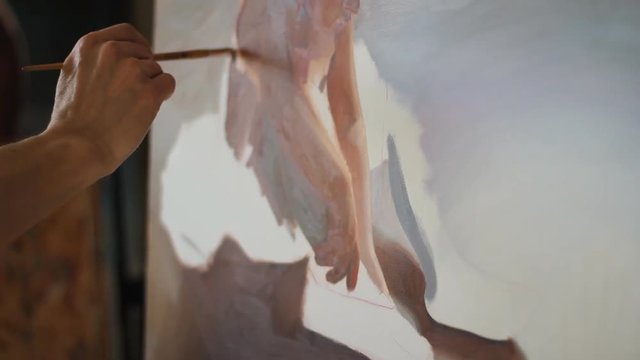 Portrait of painter in art studio. professional artist paints the picture of a little girl ballerina in a tutu and Pointe shoes. Close-up of painting the skin red, warm colour.