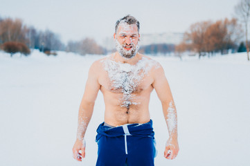 Portrait of russian bearded bodybuilder standing without clothes outdoors in winter on a frozen snowy lake with different emotions and posing for camera