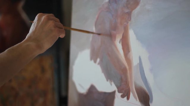 Artist working on an oil painting. View of canvas professional artist paints the picture of a little girl ballerina in a tutu and Pointe shoes. Close-up of painting the skin red, warm colour.Gaining