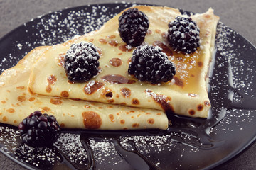 Pancakes with blackberries and honey on a black plate.
