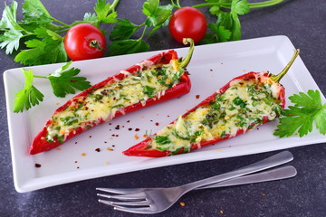 Oven cooked red paprika stuffed with cheese, garlic and herbs on a white plate with parcley and cherry tomatoes an abstract grey background. healthy eating concept. Mediterranean lifestyle.