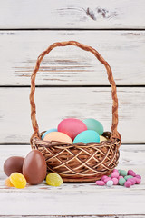 Easter egg basket and candies. Chocolate eggs on wooden surface. Easter goodies for kids.