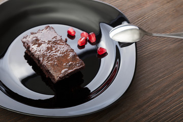 slice of brownie on black plate on a wooden table with a spoon and pomegranate seeds