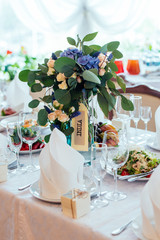 Beautiful wedding bouquet of cream roses, blue flowers and eucalyptus on the dinner table. Table setting at a luxury wedding reception. Flowers on the table