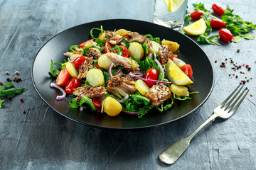 Smoked Mackerel Salad with warm boiled new potato, cherry tomatoes, chopped red onion and Ruccola on black plate.