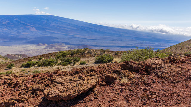 Red lava rocks on Mauna Kea, Mauna Loa in the background, colored blue from the atmosphere.