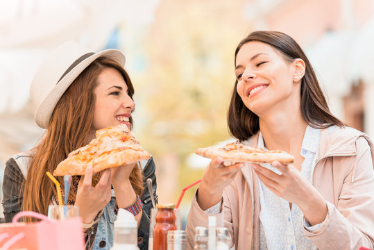 Two cheerful  girls eating pizza in a outdoor cafe