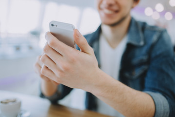 Attractive young man or freelancer with mobile is sitting in cafe and drinking coffee