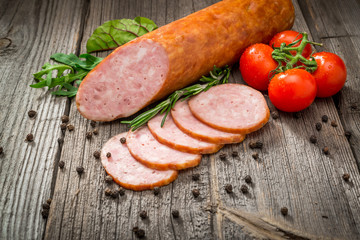 Salami sausages sliced with pepper, garlic and rosemary on cutting board on wooden table. Top view