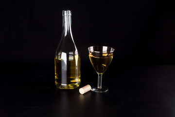 Open bottle of white wine and a glass of wine on a black background